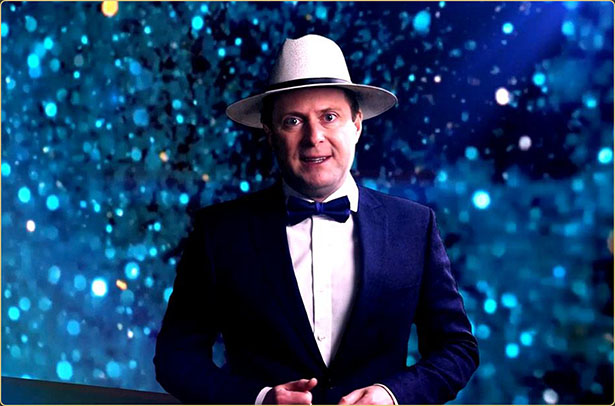 Arek Zasowski hosting Actors by Actors Show — Award-Winning Interview Series Arek Zasowski dressed in a tuxedo and fedora, standing against a blue cinematic bokeh background while hosting an episode of the Actors by Actors Show