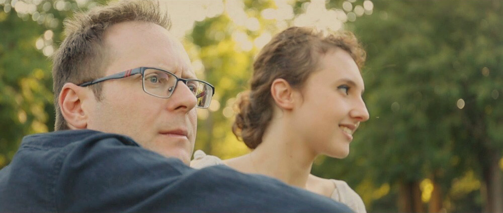 Arek Zasowski in The Cure student film, sitting outdoors beside a young woman in warm sunlight, emotional and cinematic moment showcasing early acting performance.