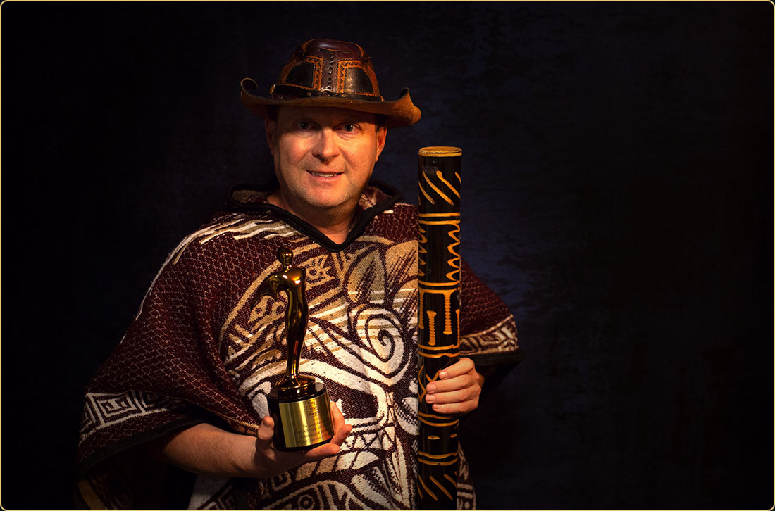 Gold Telly Award Winner — Adventure, fantasy, and filmmaking magic come to life Award-winning filmmaker Arek Zasowski in a tribal poncho and adventure hat, proudly holding his Gold Telly Award and rainstick—evoking cinematic adventure and global storytelling