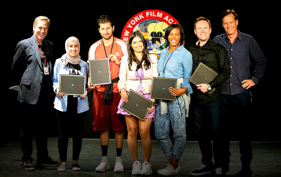 Arek Zasowski at the New York Film Academy Acting for Film workshop graduation in Los Angeles, standing with fellow actors and instructors Martin Thompson and Bruce MacWilliams on stage, holding certificates, NYFA logo visible behind.